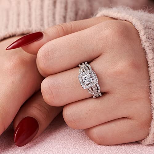 Close-up of a hand wearing a diamond ring with red nail polish.